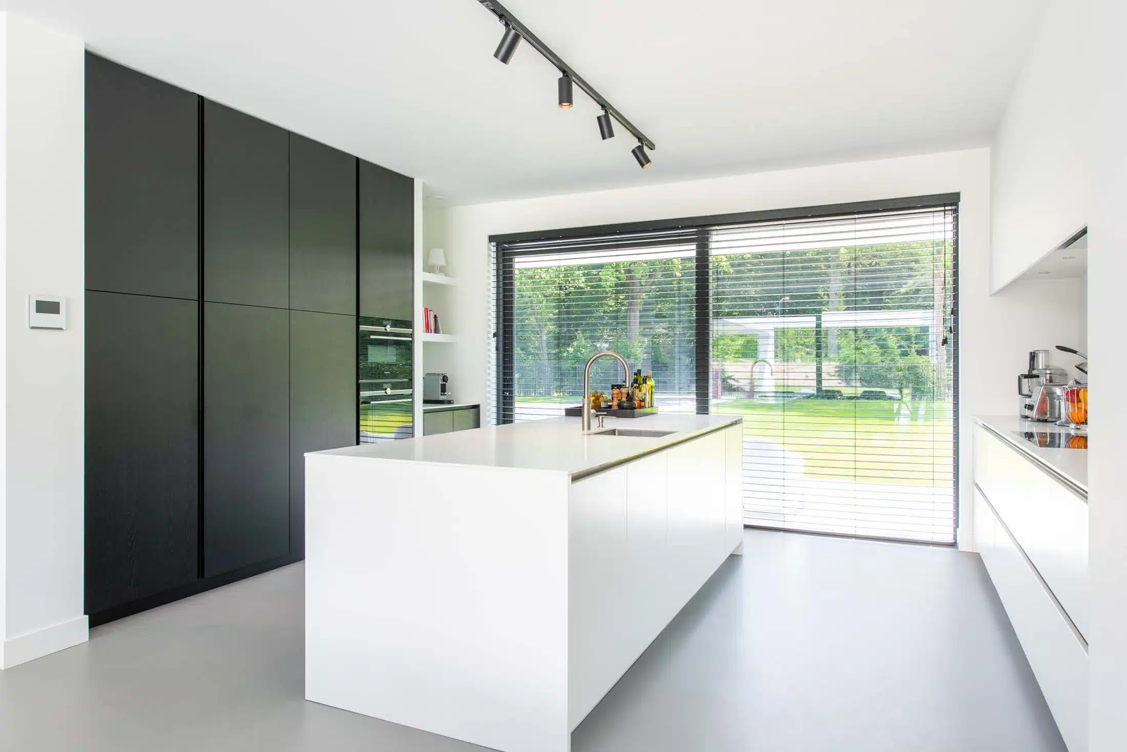 Minimalistische keuken met een strak design en een groot wit eiland voorzien van een ingebouwde inductiekookplaat en wijnkoeler. De witte matte kasten combineren perfect met de natuurlijke houten plafonddetails, wat warmte en eenvoud toevoegt.