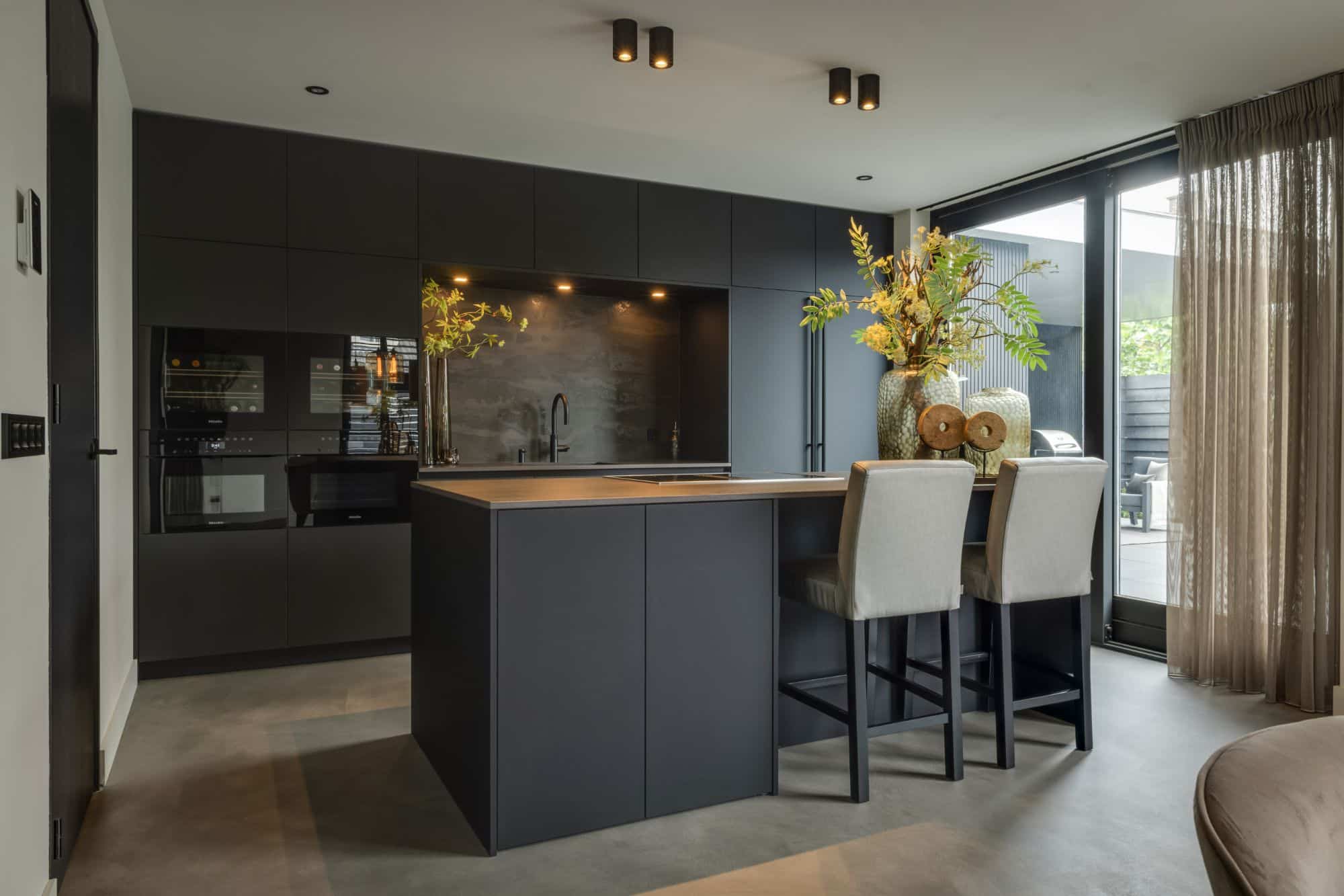 Overzicht van een luxe keuken met nis en kookeiland in Rotterdam, uitgevoerd in Fenix-mat zwart met een keramisch werkblad