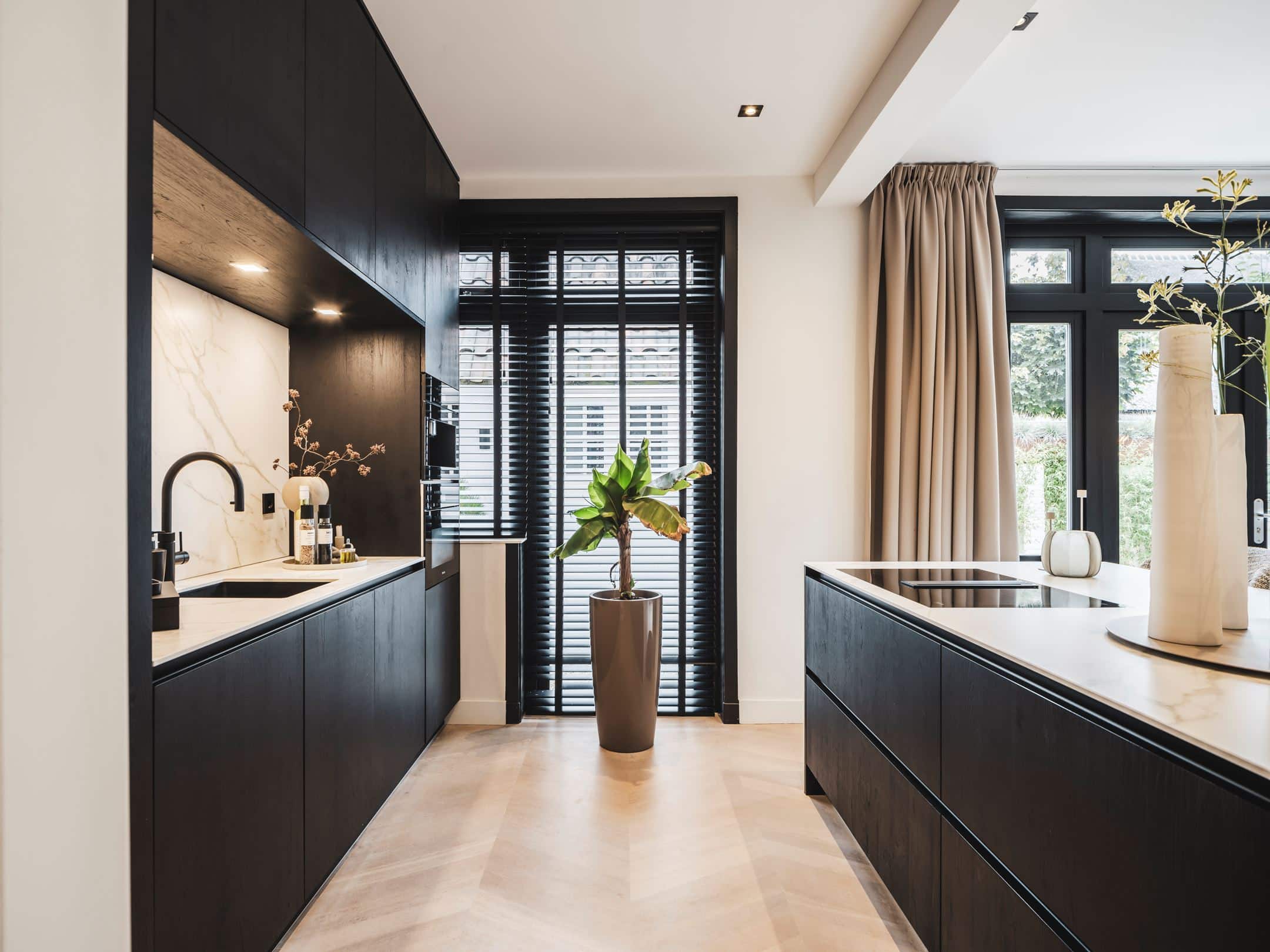 Luxe zwarte keuken met zwarte fronten en een marmerlook werkblad. De keuken beschikt over een strak kookeiland, ingebouwde apparatuur en een stijlvolle nis met verlichting.