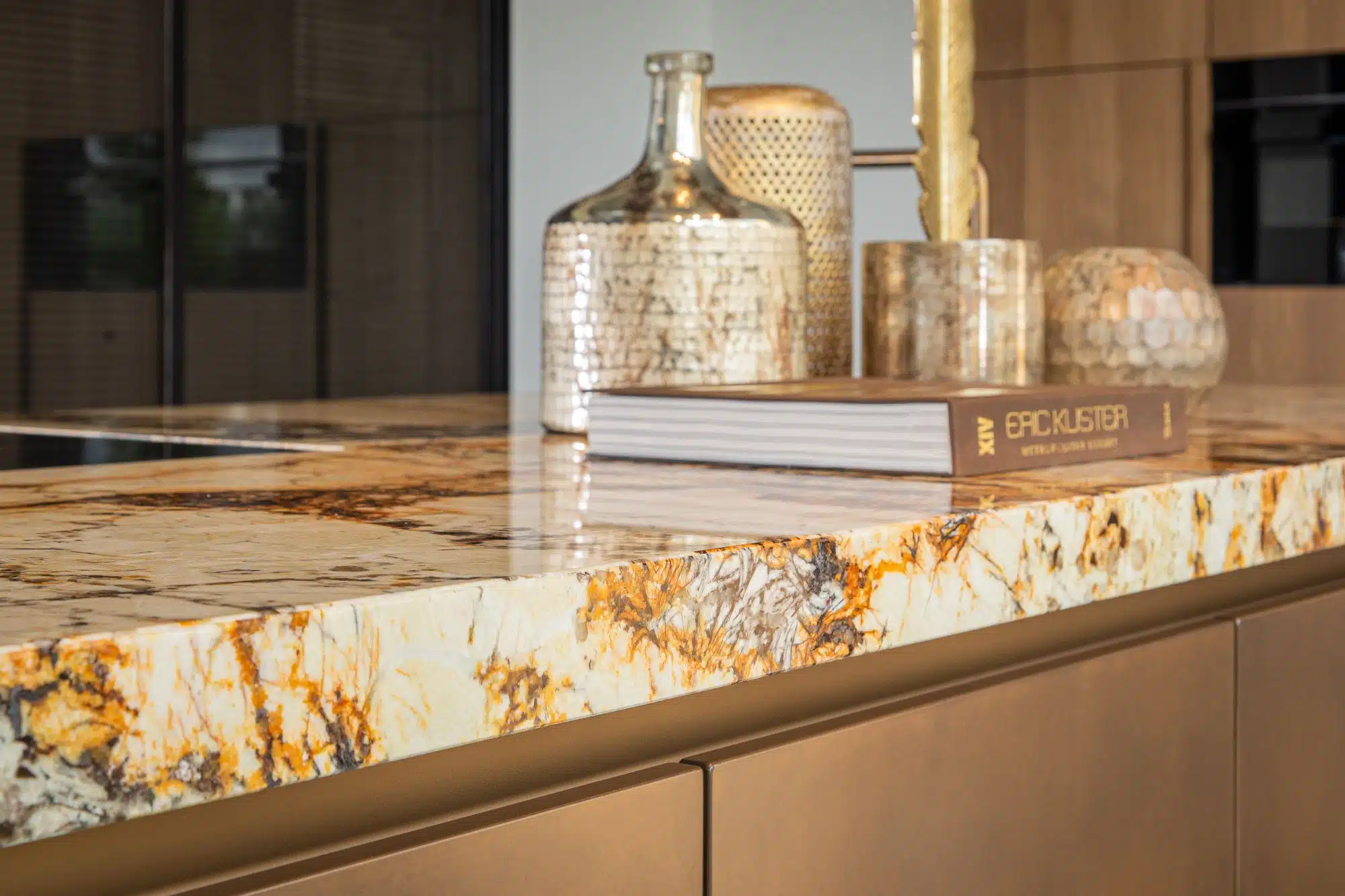 Luxe keukeneiland met een opvallend Patagonia kwartsiet blad, gedecoreerd met stijlvolle gouden accessoires en een interieurboek