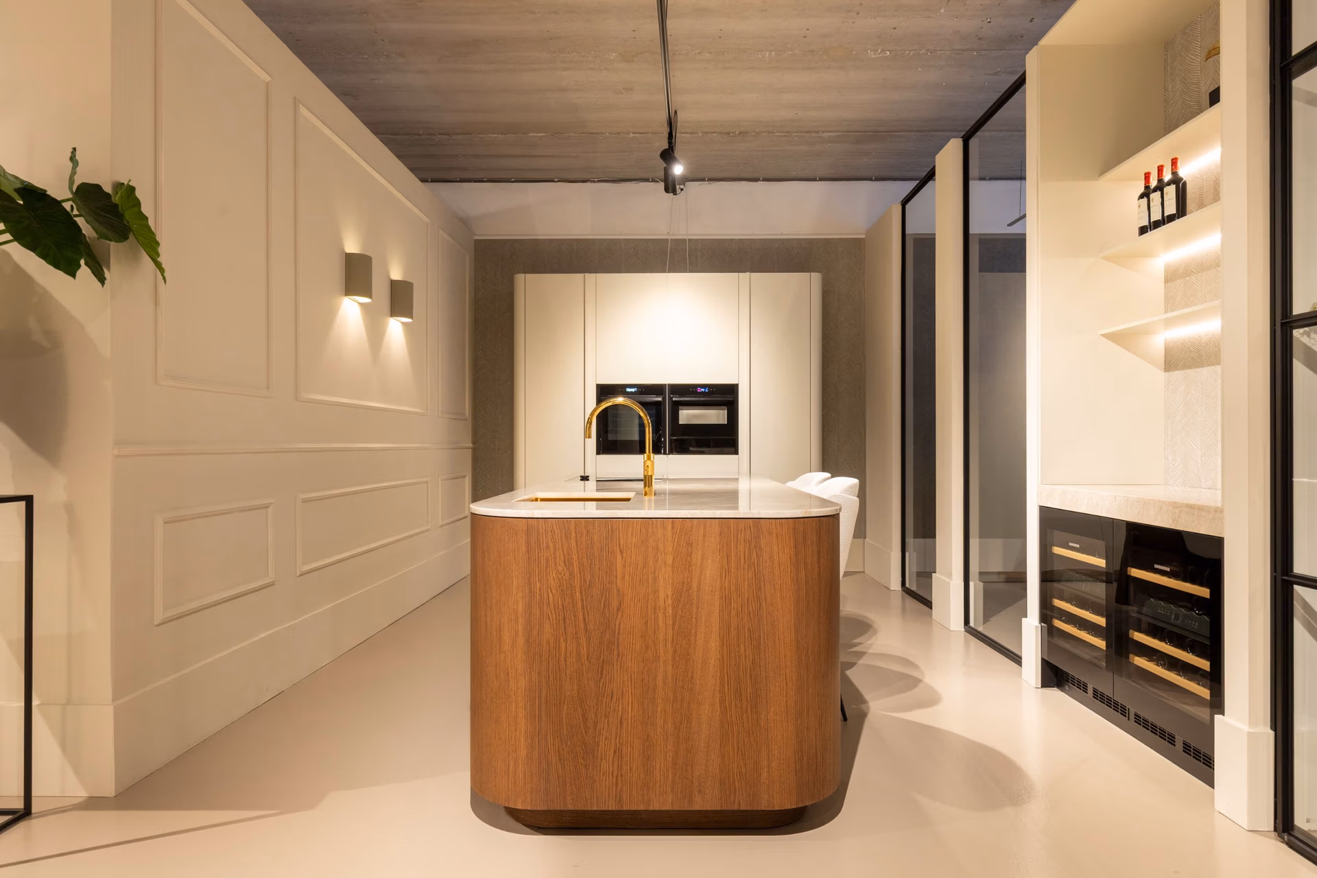 Modern Japandi keukeninterieur in de showroom van By Sensa, met een centraal keukeneiland van hout en marmeren blad, goudkleurige kraan, ingebouwde ovens en minimalistische afwerking in warme tinten.